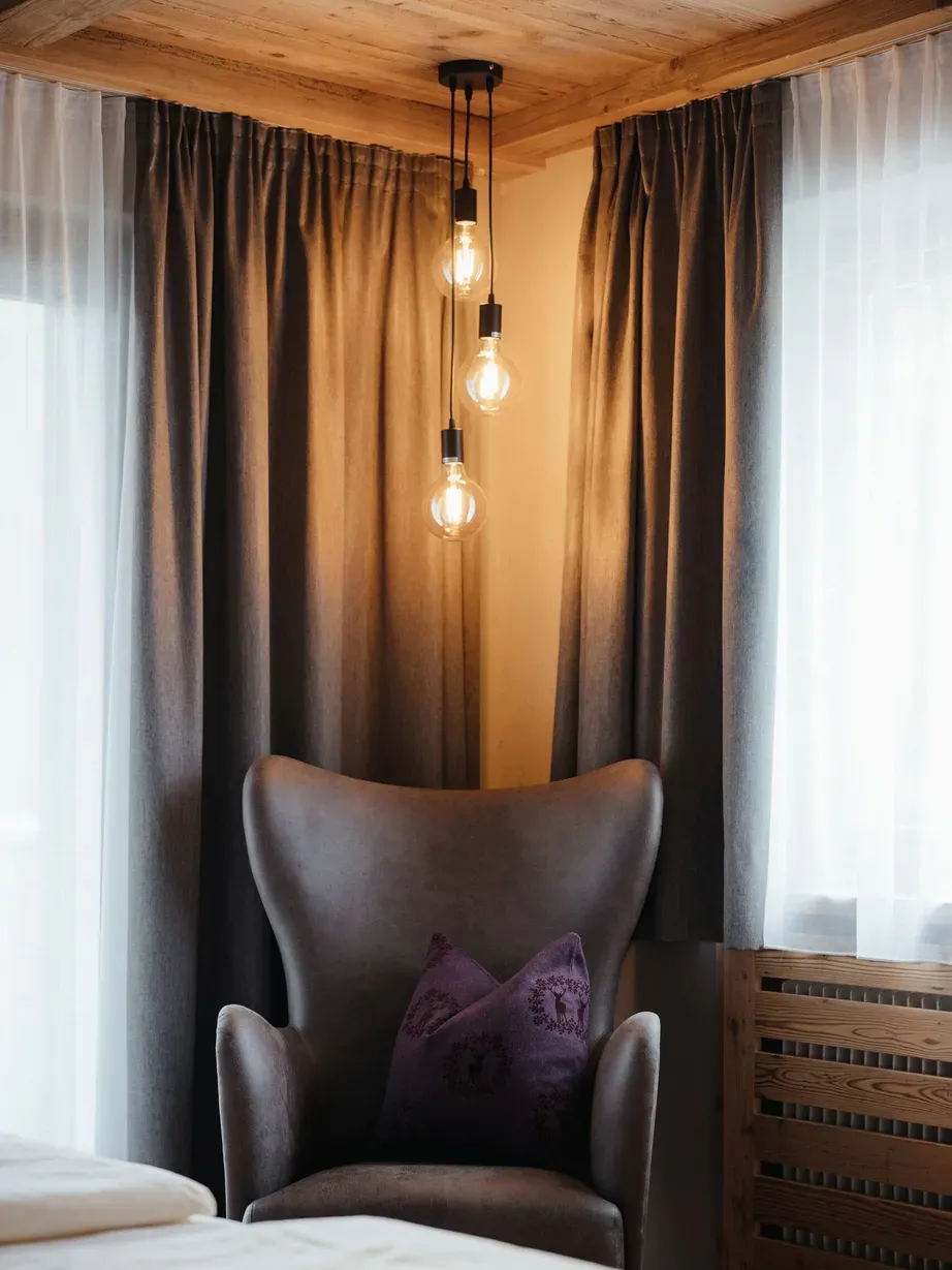 Hotel Gran Ander: brauner Leder-Armstuhl mit violettem Kissen, drei hängende Glühbirnen, dunkle Vorhänge, helle Fensterseite, Holzdeckenbalken.