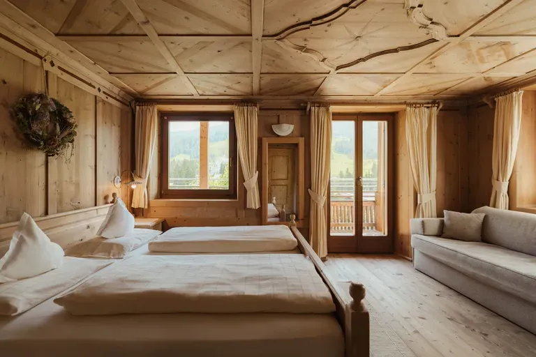 Camera da letto in legno, Hotel Gran Ander, Badia: letto matrimoniale, divano beige, finestre e balcone con vista sulle Dolomiti.
