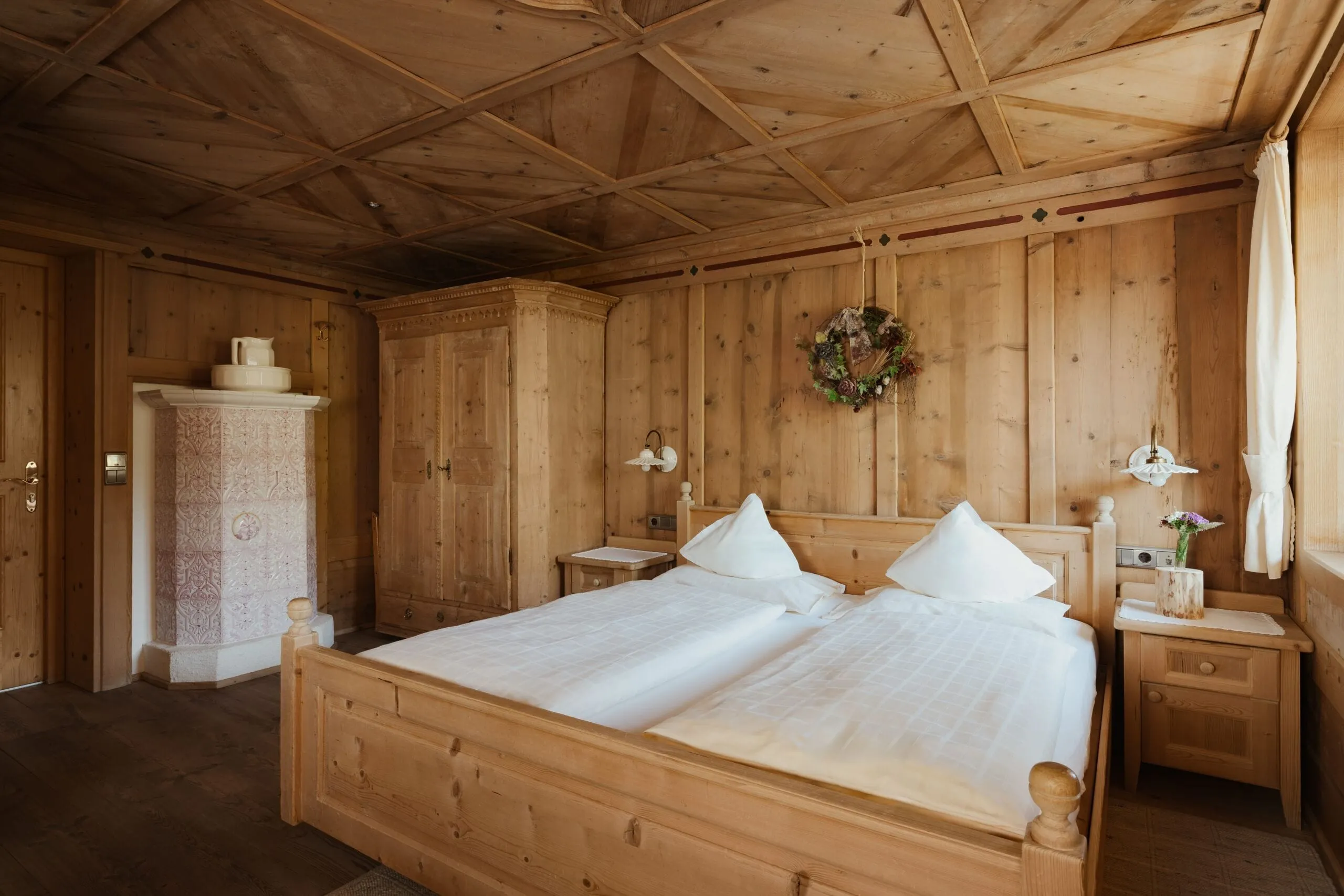 Hotelzimmer im Holzstil im Hotel Gran Ander, Badia: massives Bett, zwei Nachttische, Garderobe, Wandkranz, Holzverkleidung und Fenster mit Vorhängen.