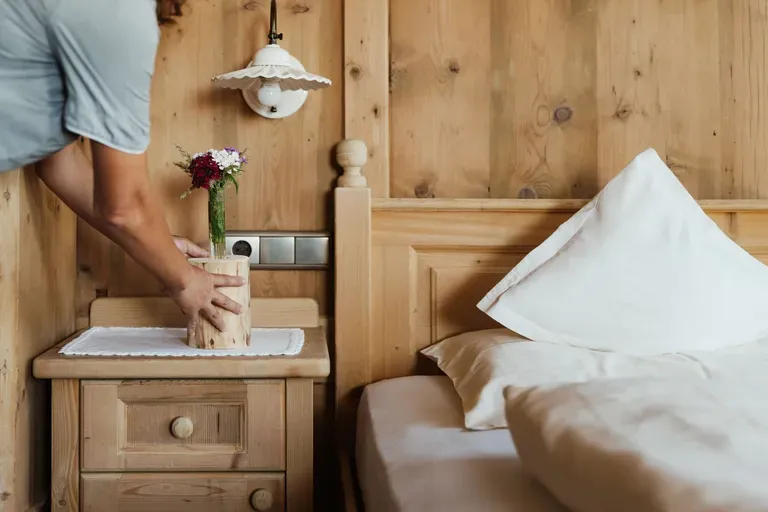 Person platziert eine Holzvase mit Blumen auf dem Nachttisch neben dem Bett in einem rustikalen Holzzimmer des Hotel Gran Ander in Badia, Alta Badia.