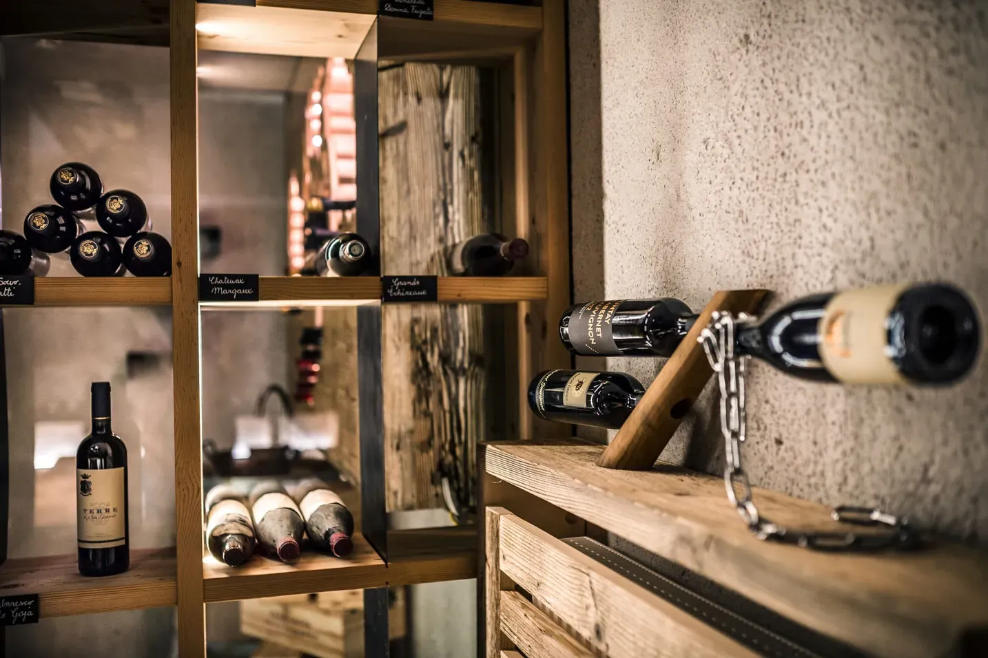 Cantina dell'Hotel Gran Ander, Badia (Alta Badia, Dolomiti): scaffali in legno con bottiglie di vino allineate, luce calda e parete di pietra.