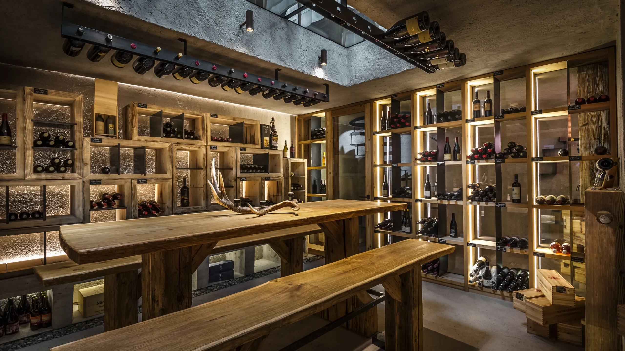 Cantina interna dell'Hotel Gran Ander, Badia: tavolo e panche in legno massiccio, scaffali a muro con bottiglie di vino e illuminazione calda.
