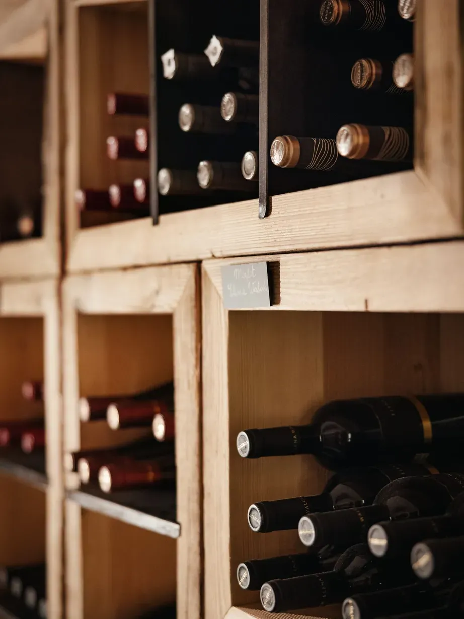 Wooden wine racks filled with bottles laid horizontally, warm lighting highlighting corks and glass in a rustic cellar.