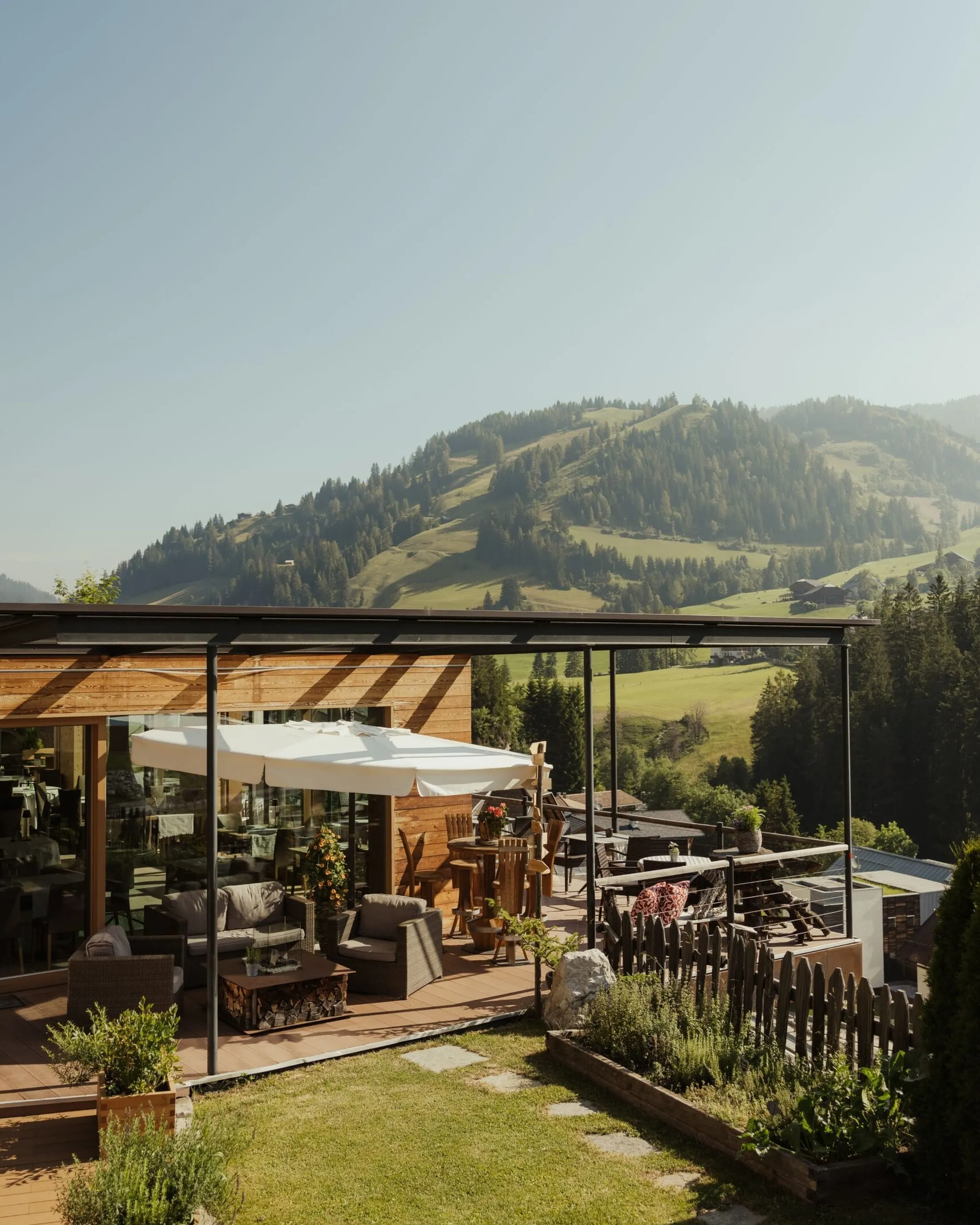 Hotel Gran Ander terrace in Alta Badia, Dolomites: glass-walled wooden deck with lounge seating, white umbrellas, and a mountain valley view.