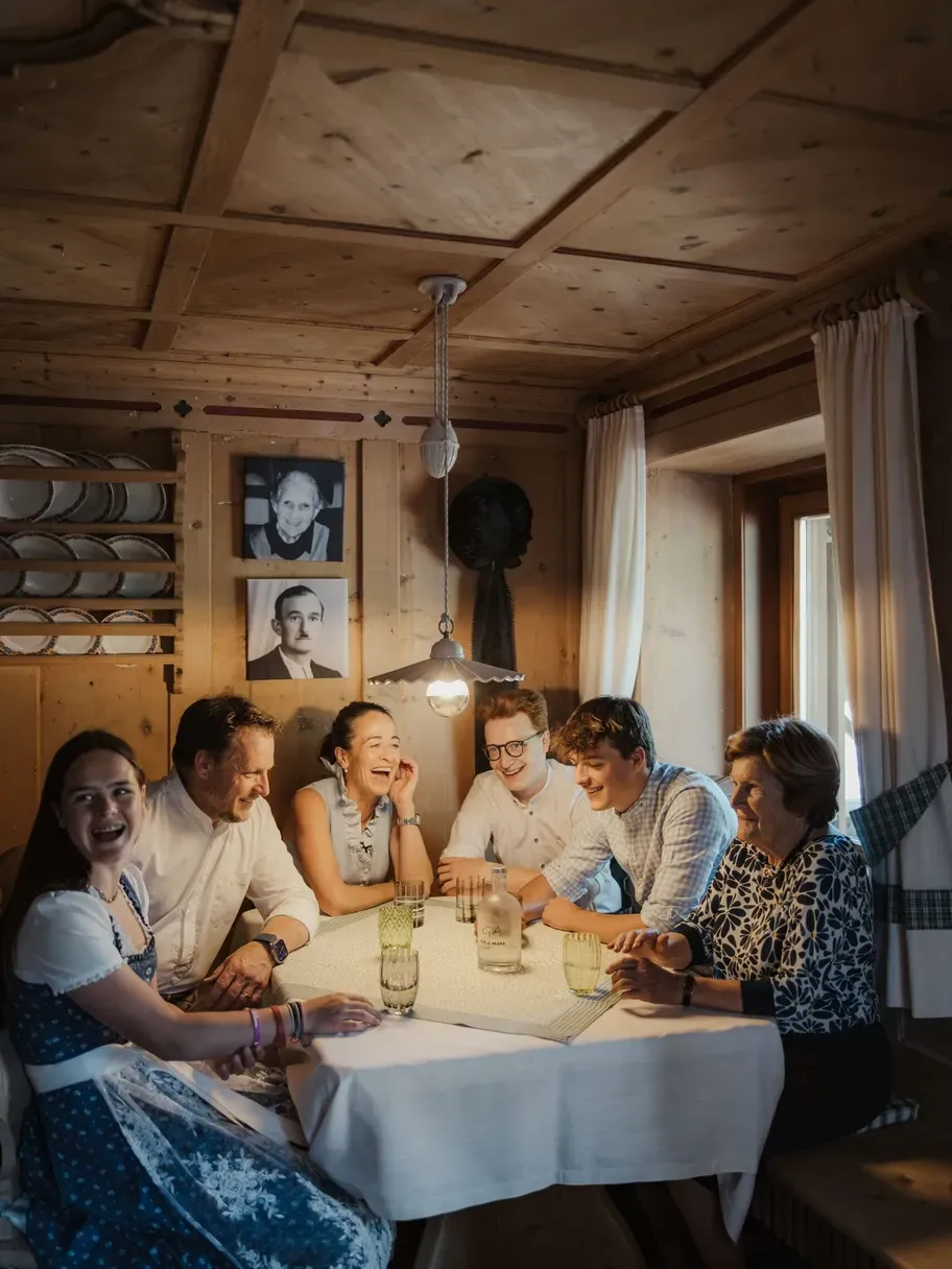 Family Irsara sit around a wooden dining table in the Hotel Gran Ander dining room, laughing under a hanging lamp.