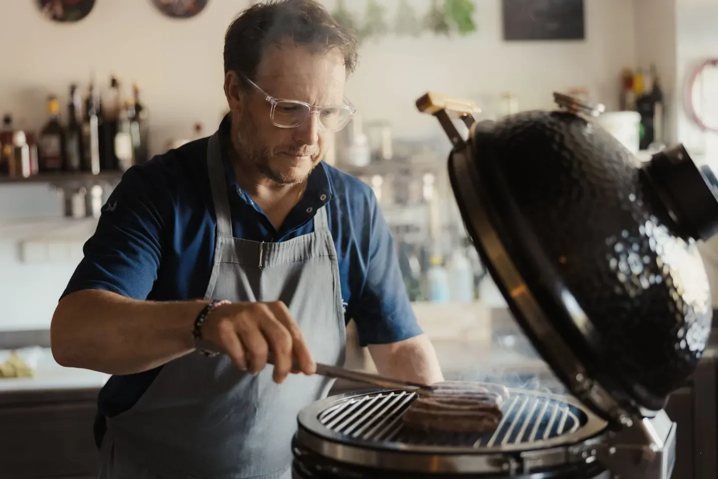 Andrea cooks on a barbecue, flipping a burger on the grill in a restaurant kitchen.
